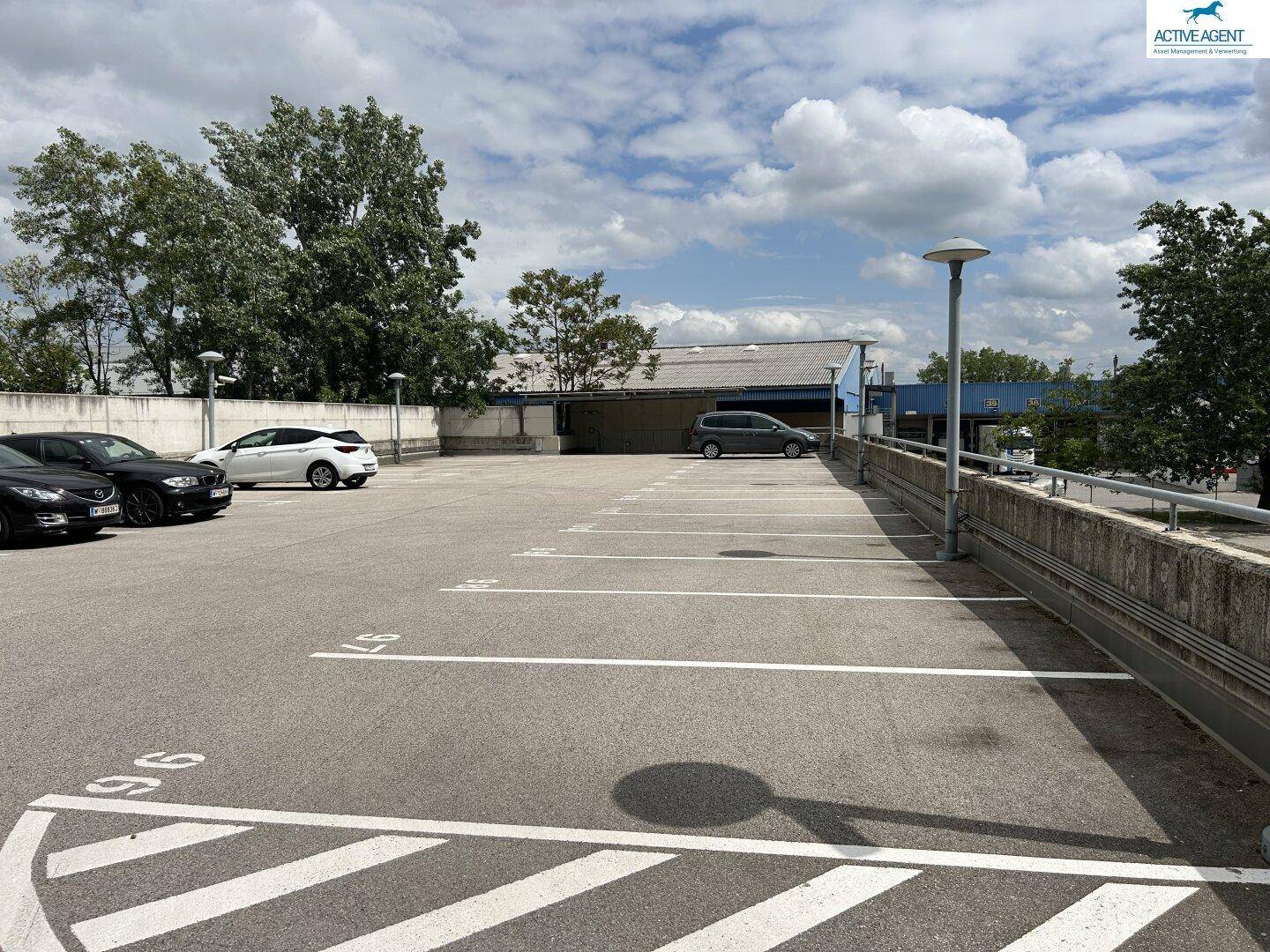 Oberirdisches Parkdeck mit markierten Stellplätzen und einer Betonmauer, unter einem teilweise bewölkten Himmel.