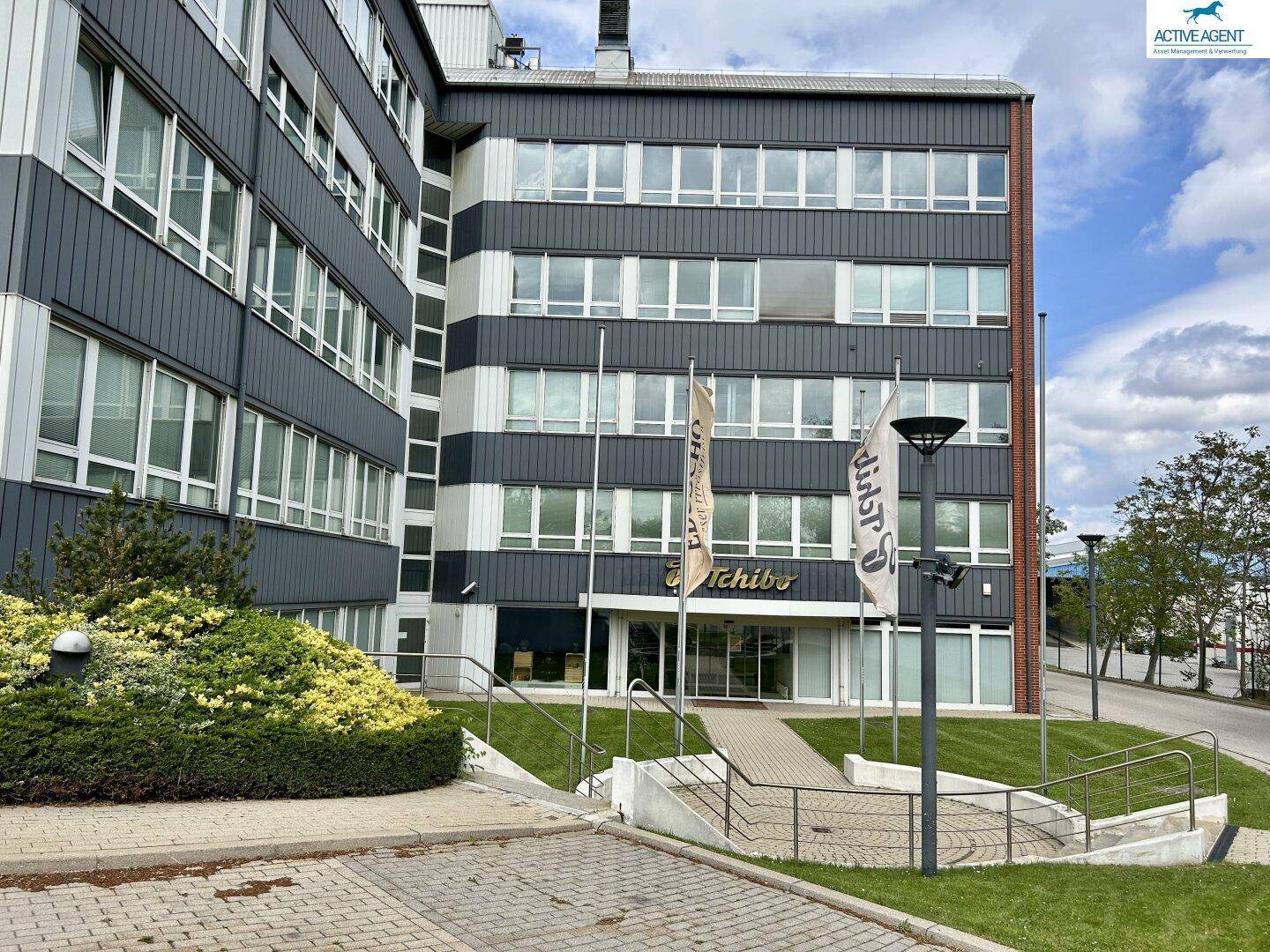 Ansicht des Bürogebäudes mit markanter gestreifter Fassade, großen Fenstern und gepflegter Grünfläche im Vordergrund.