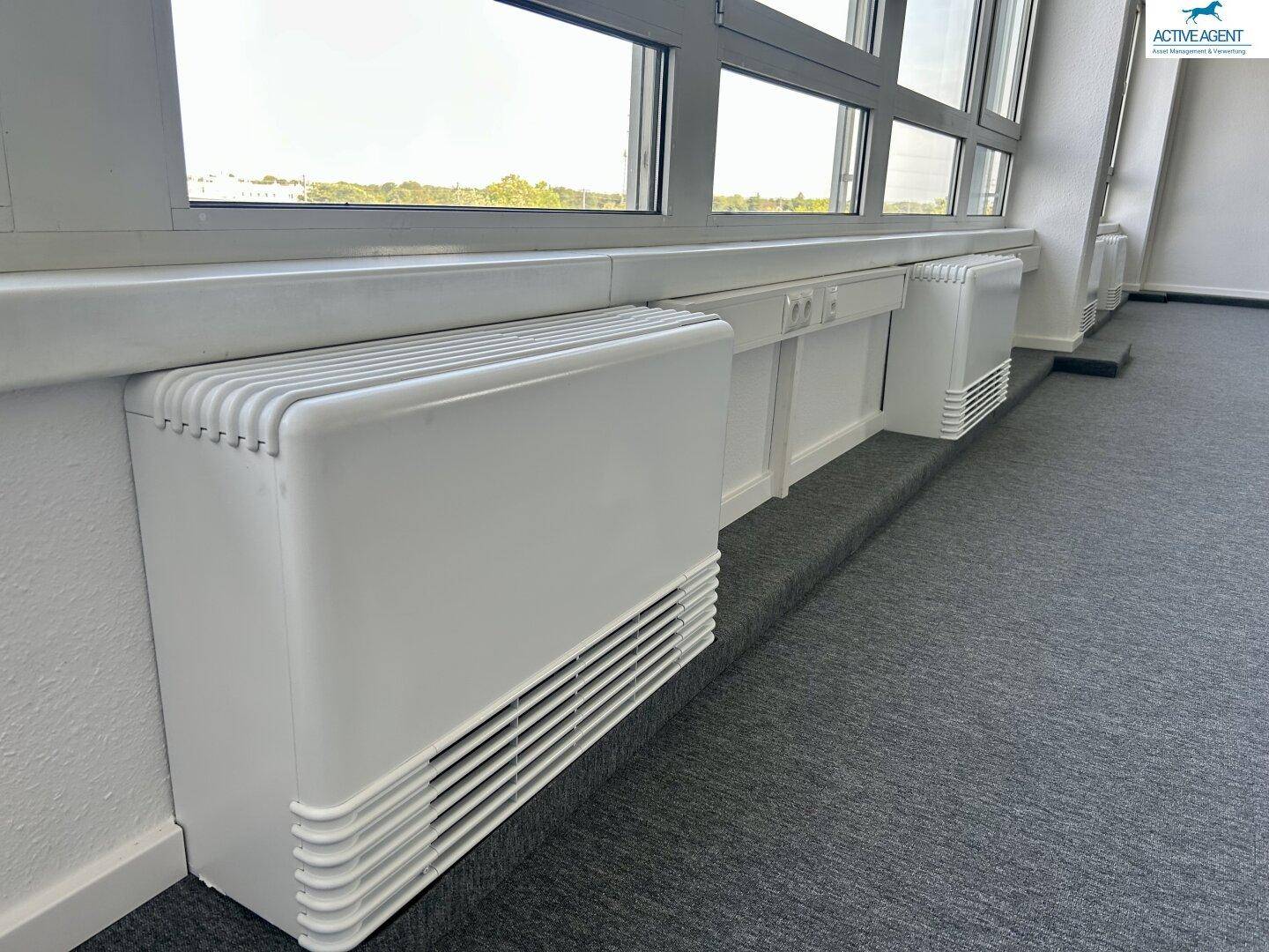 Detailansicht der Heizkörper unter den großen Fenstern in einem modernen Büroraum.