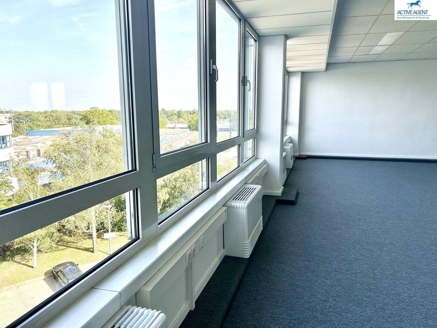 Heller Büroraum mit einer Fensterfront, die einen weiten Blick ins Grüne und auf die Umgebung bietet.