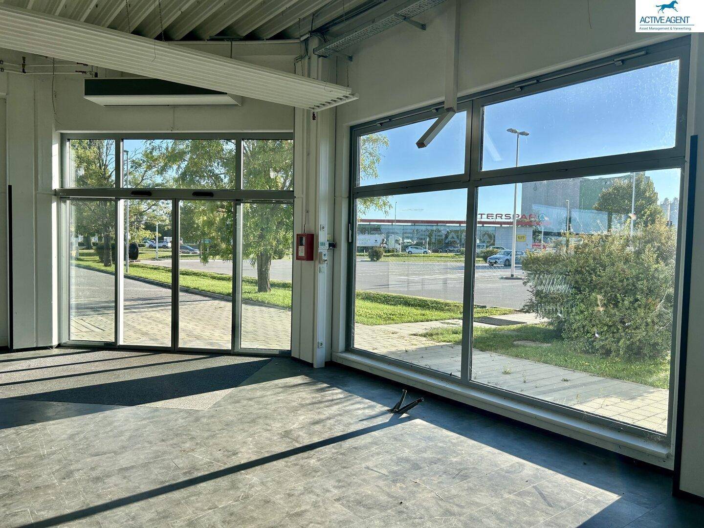Blick vom Innenraum durch die großen Glasfenster auf den Parkplatz und die umliegenden Gebäude.
