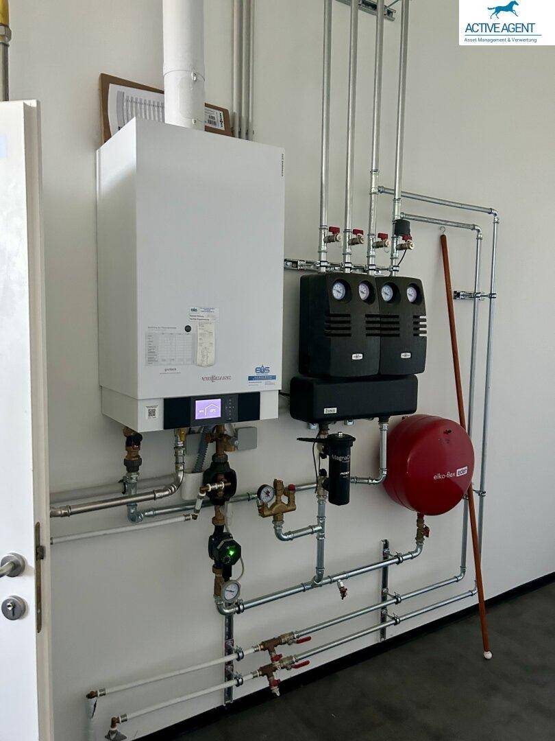 Moderner Heizungsraum mit Gastherme, umfangreicher Verrohrung und einem roten Ausdehnungsgefäß an der Wand.
