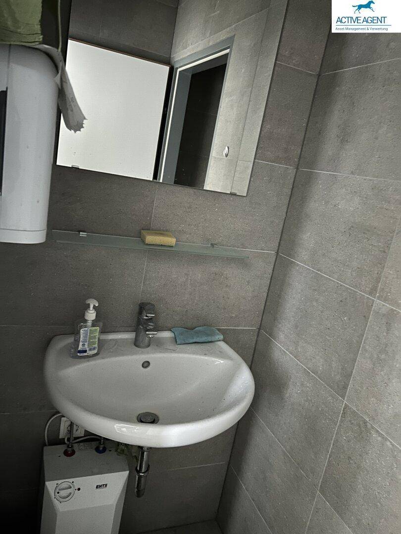 Kleines Badezimmer mit Waschbecken, Spiegel und modernen grauen Fliesen an Wänden und Boden.