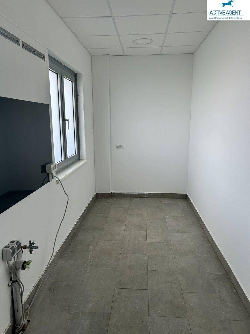 Kleiner Büroraum mit Fenster, weißen Wänden und grauen Fliesen, ideal für Einzelarbeitsplätze.