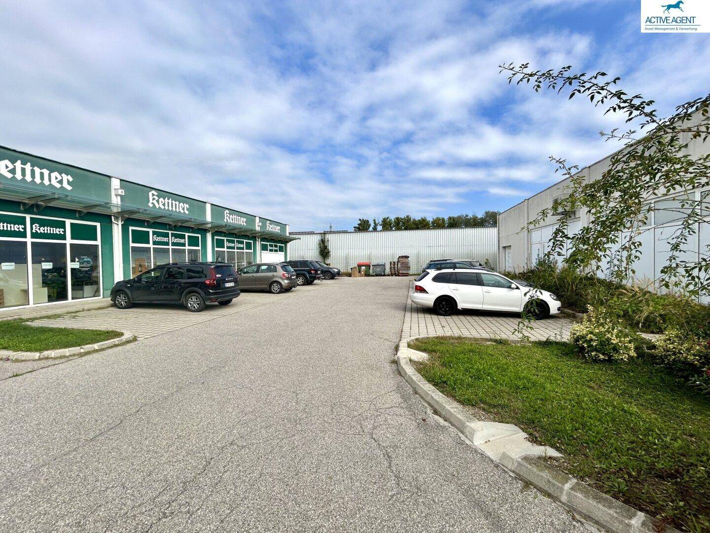 Außenansicht eines Geschäftsgebäudes mit "Kettner"-Schildern und einem Parkplatz davor, umgeben von Grünflächen.