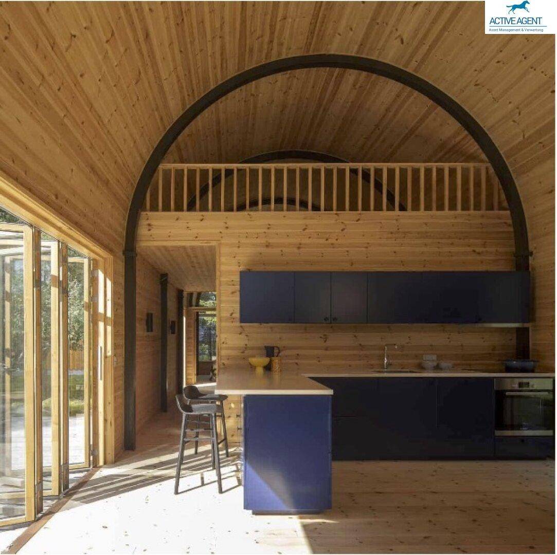 Moderne Holzküche mit dunklen Schränken, Kochinsel und offener Galerie unter gewölbter Decke.