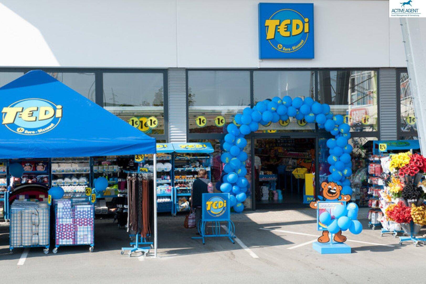 Eingangsbereich eines Tedi-Geschäfts mit blauer Dekoration, Ballonbogen und Verkaufsständen im Freien.