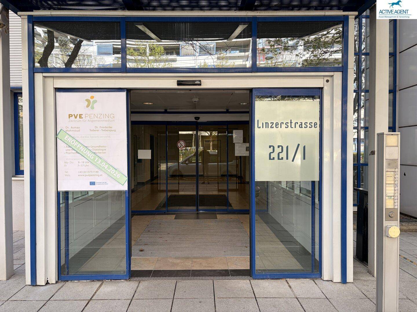 Eingangsbereich eines modernen Bürogebäudes mit großen Glastüren und Beschilderung, die den Zugang zum Gebäude anzeigt.