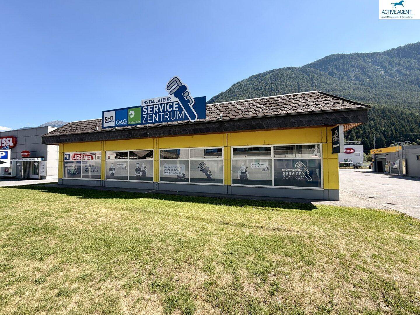 Gelbes Geschäftsgebäude mit Servicezentrum-Beschilderung, umgeben von einer Wiese und Parkplätzen.