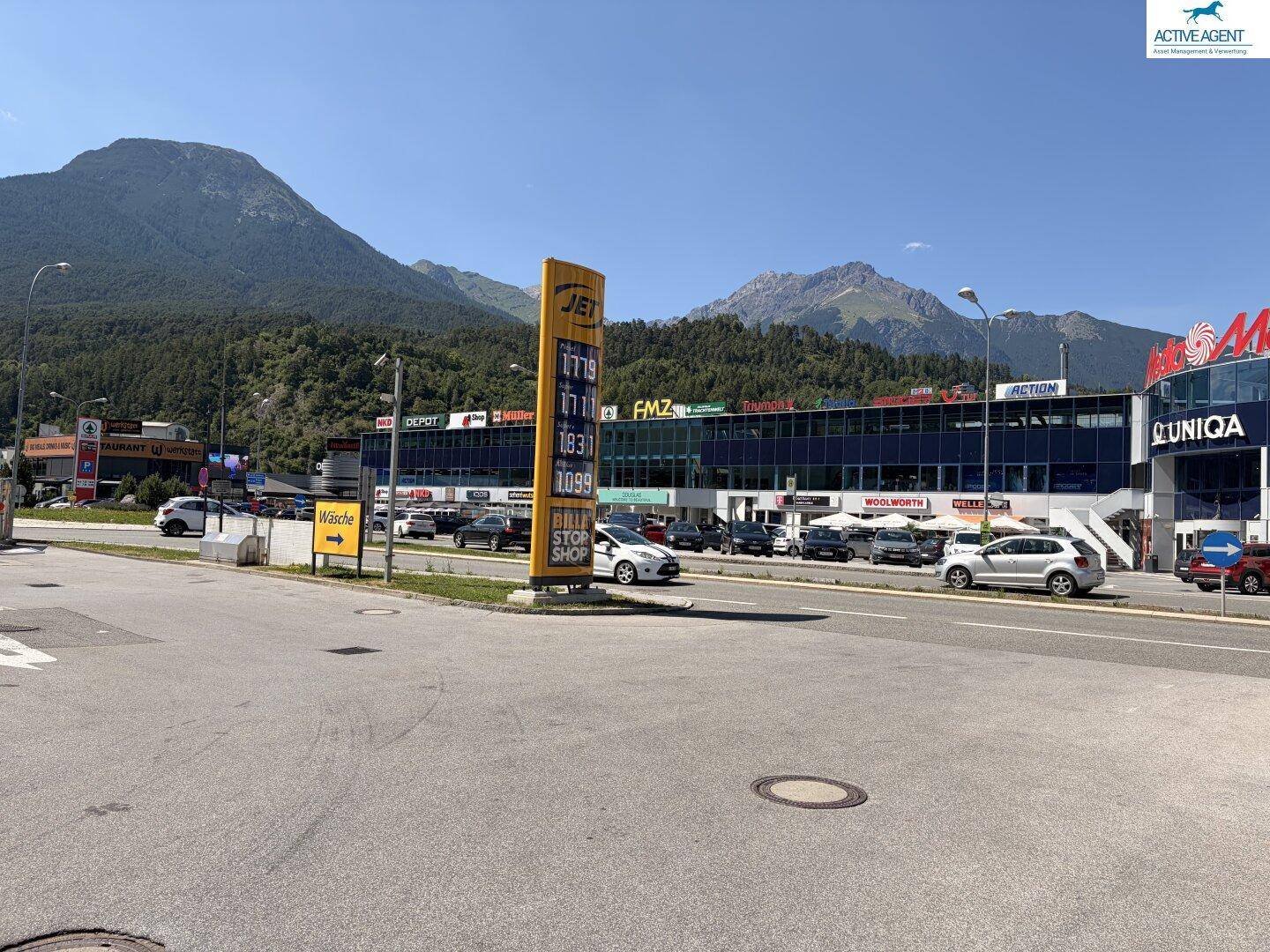 Weitwinkelaufnahme der kommerziellen Umgebung mit Tankstelle, Einkaufszentrum und Bergpanorama.