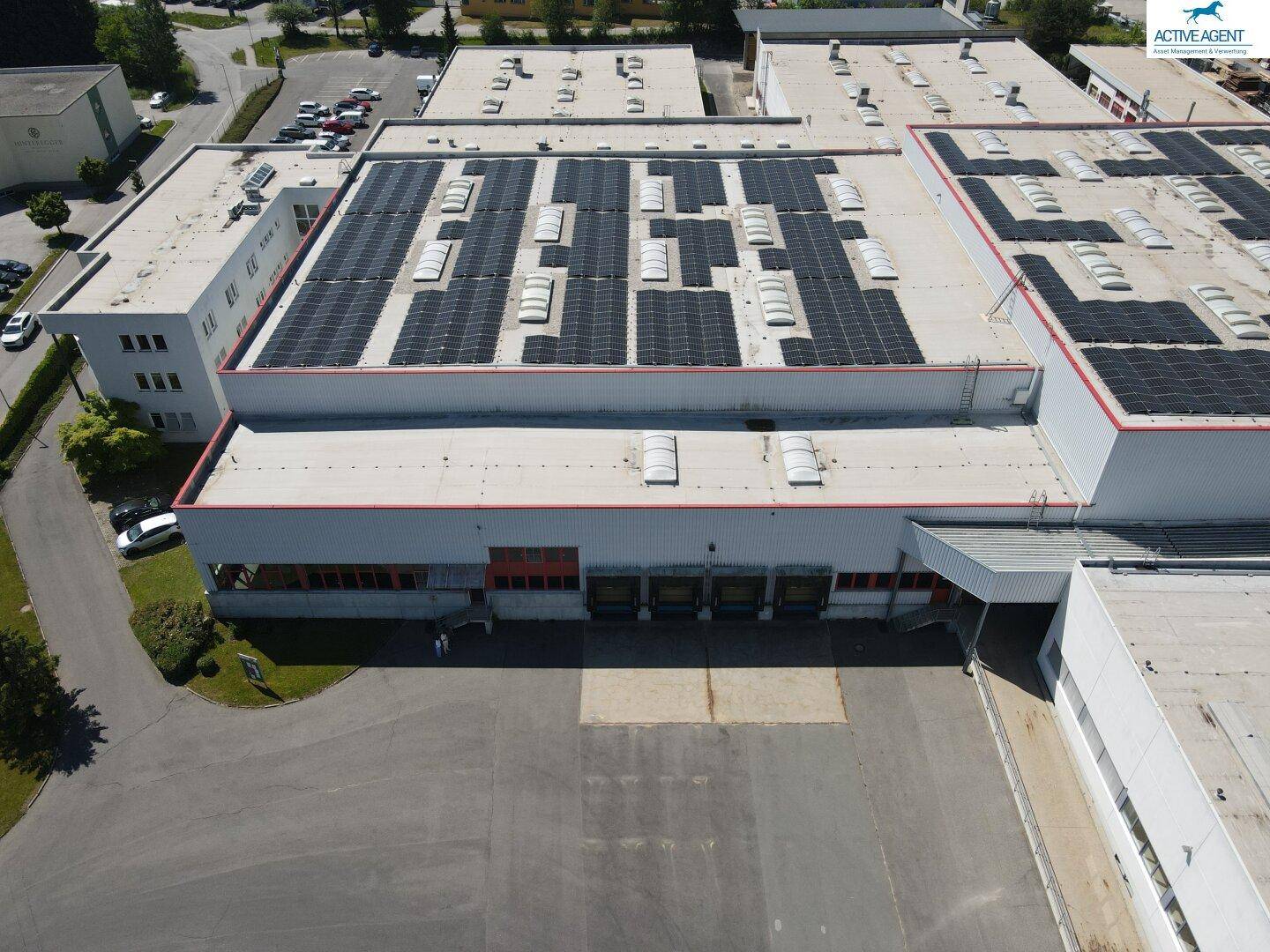 Vogelperspektive auf ein Industriegebäude mit zahlreichen Solarmodulen auf dem Dach und Laderampen.