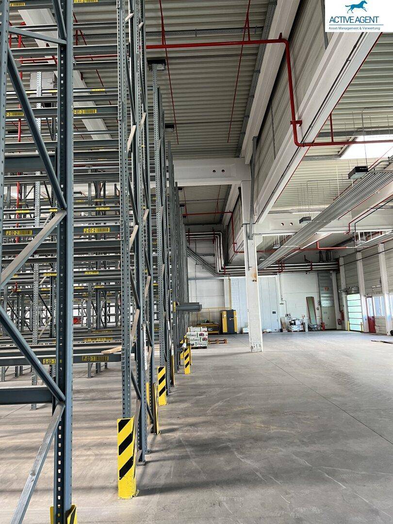Industrielle Lagerhalle mit hohen Regalsystemen und sichtbaren Lüftungsrohren an der Decke.