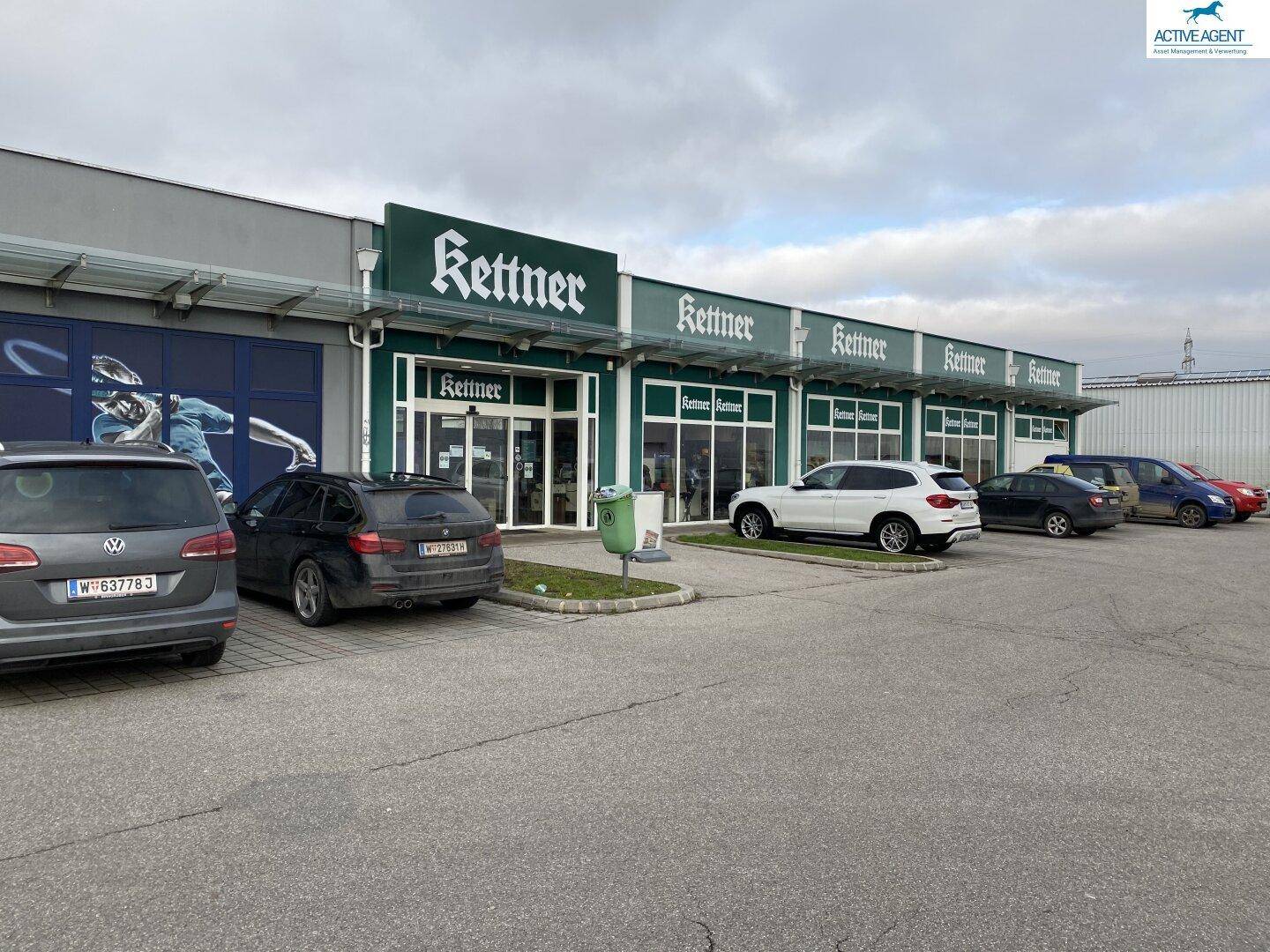 Gewerbegebäude mit der Aufschrift 'Kettner' und mehreren geparkten Autos auf dem Parkplatz.
