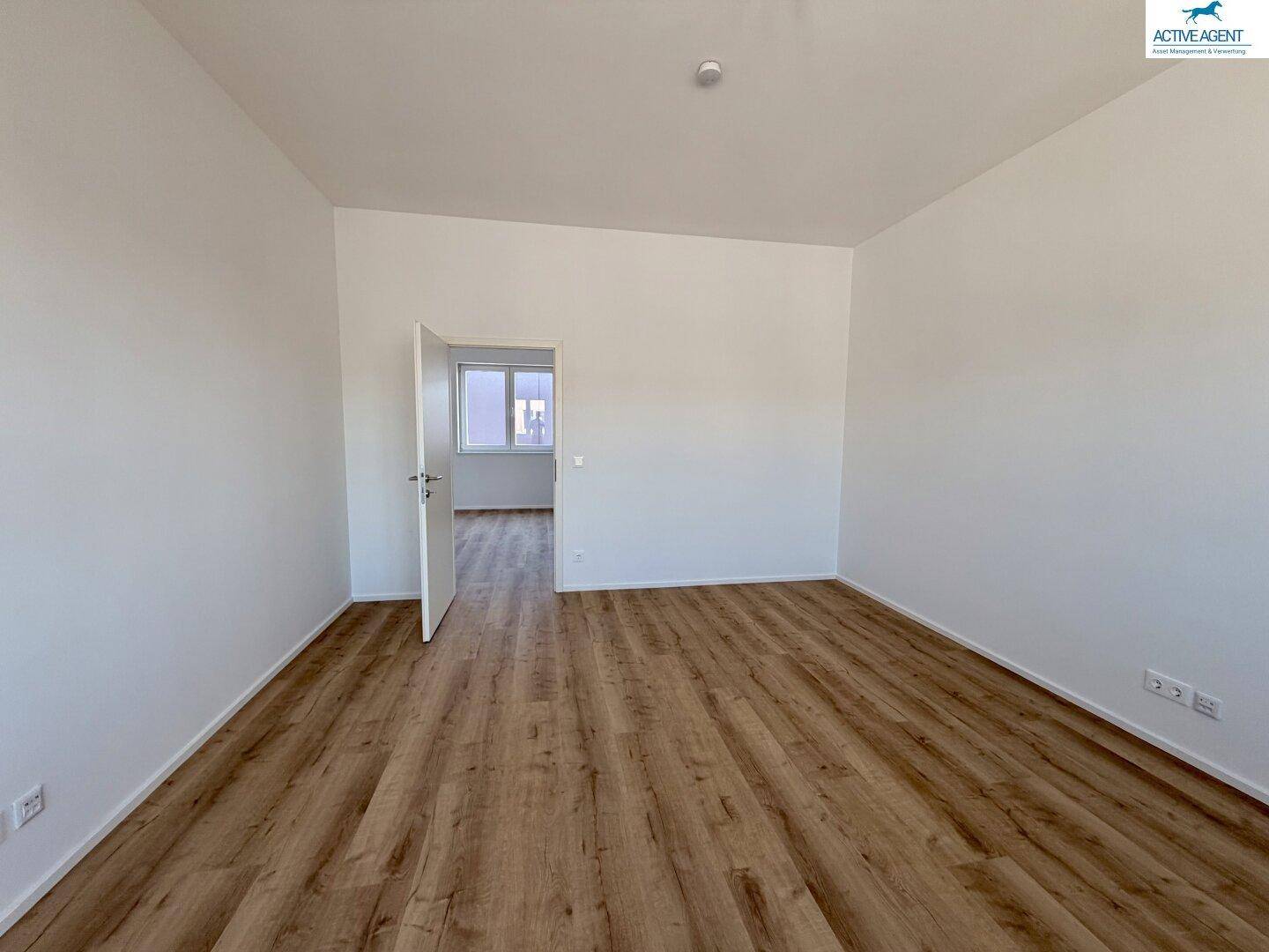 Leeres Zimmer mit hellem Laminatboden und weiß gestrichenen Wänden, bereit zum Einzug.