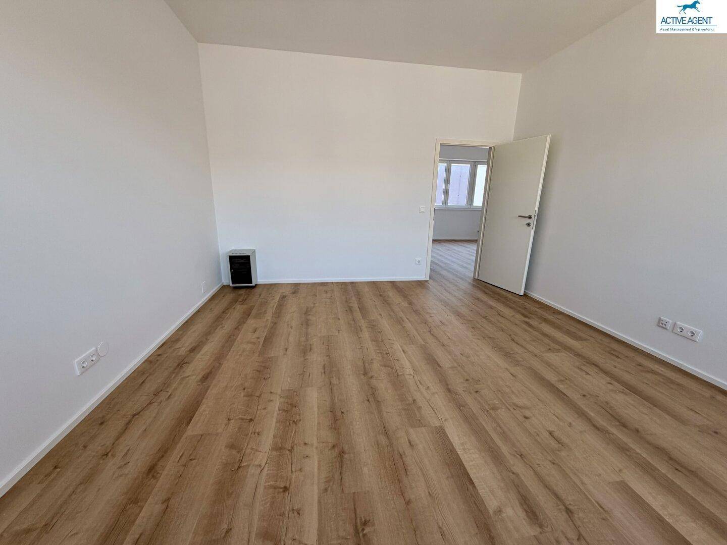 Unmöbliertes Zimmer mit modernem Laminatboden und weißen Wänden, ideal für verschiedene Nutzungen.