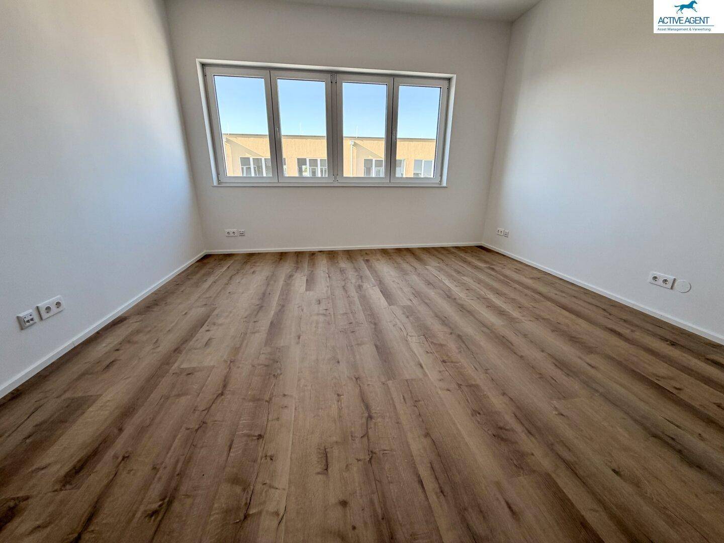 Helles Zimmer mit großem Fenster, Laminatboden und weiß gestrichenen Wänden, bietet viel Tageslicht.