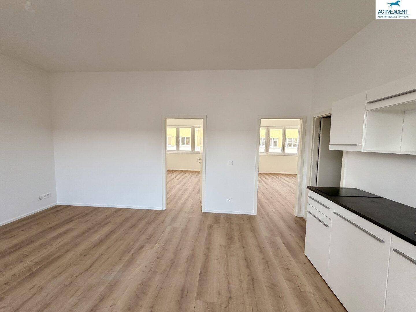 Offener Wohnbereich mit Laminatboden und Zugang zu weiteren Zimmern, ideal für flexible Gestaltung.
