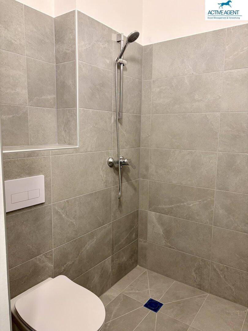 Modernes Badezimmer mit grauen Fliesen, ebenerdiger Dusche und wandhängendem WC.