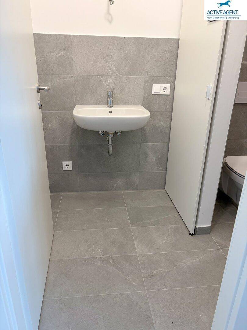 Helles Badezimmer mit modernem Waschbecken, grauen Fliesen und weißer Tür.