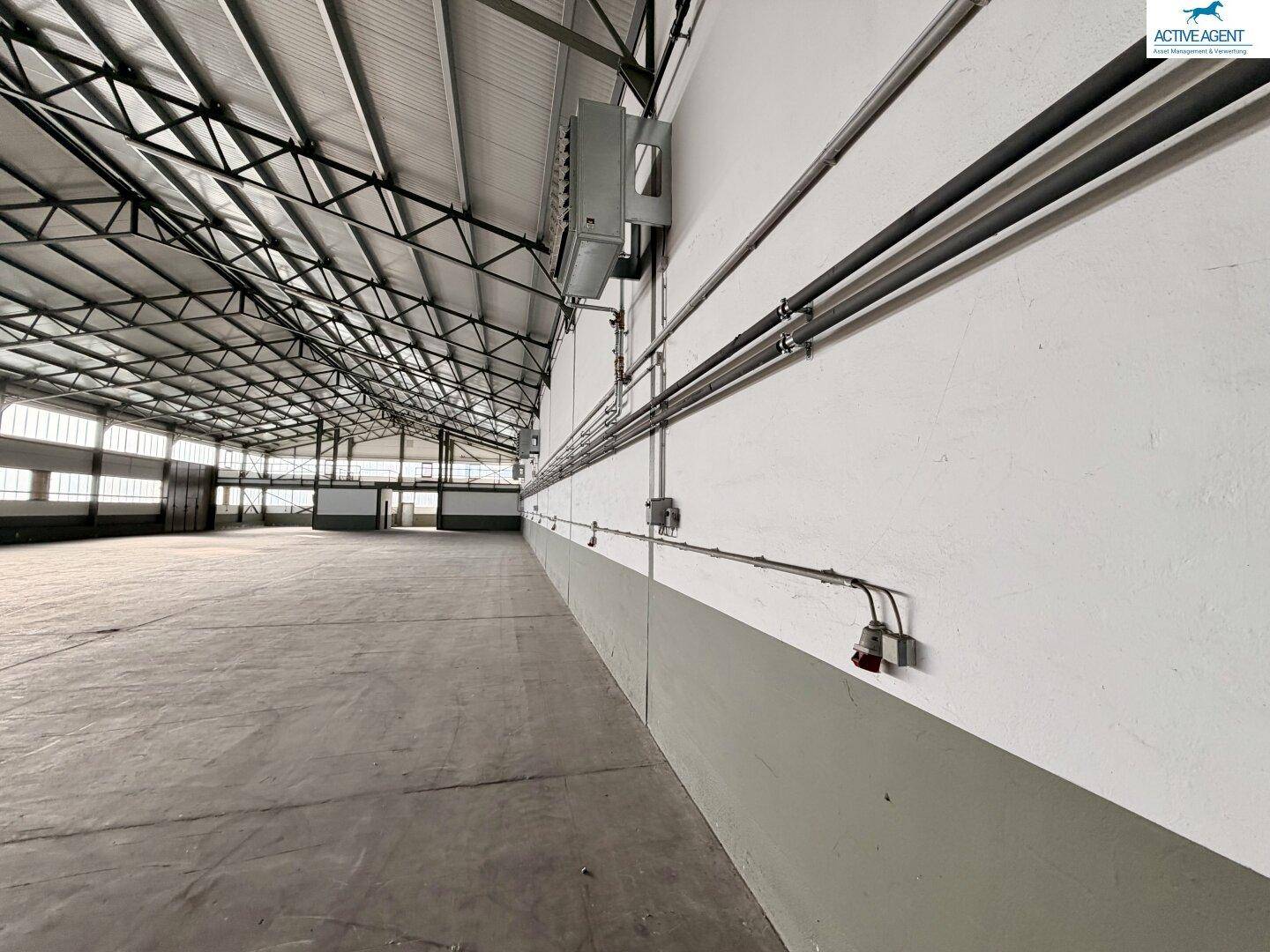 Lange Wand in der Lagerhalle mit sichtbaren Installationen und hoher Decke, in gutem Zustand.