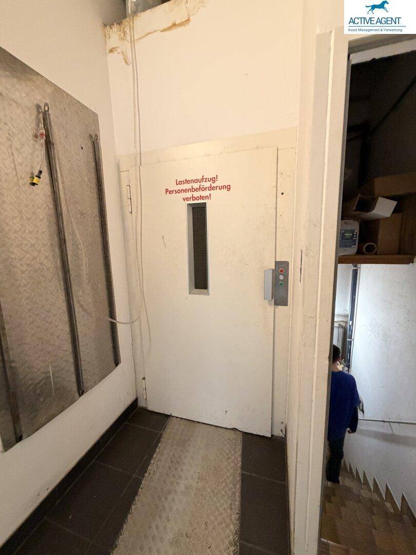 Lastenaufzug mit Warnhinweis, daneben eine Treppe, die zu weiteren Etagen führt.