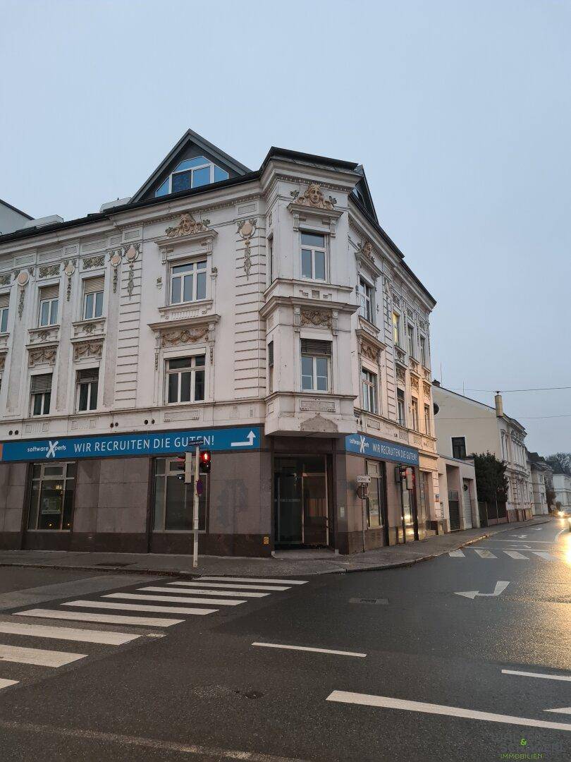 Historisches Eckgebäude bei Dämmerung, beleuchtet an einer städtischen Kreuzung mit Zebrastreifen.