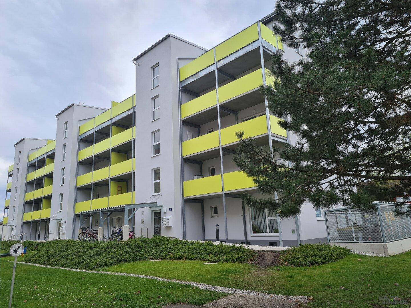 Modernes Mehrfamilienhaus mit auffälligen gelb-grünen Balkonen und gepflegter Grünanlage.