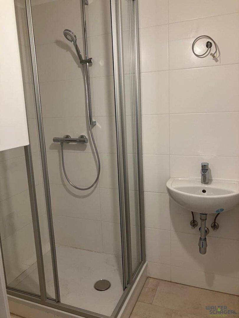 Badezimmer mit Duschkabine, kleinem Waschbecken und weißen Fliesen.