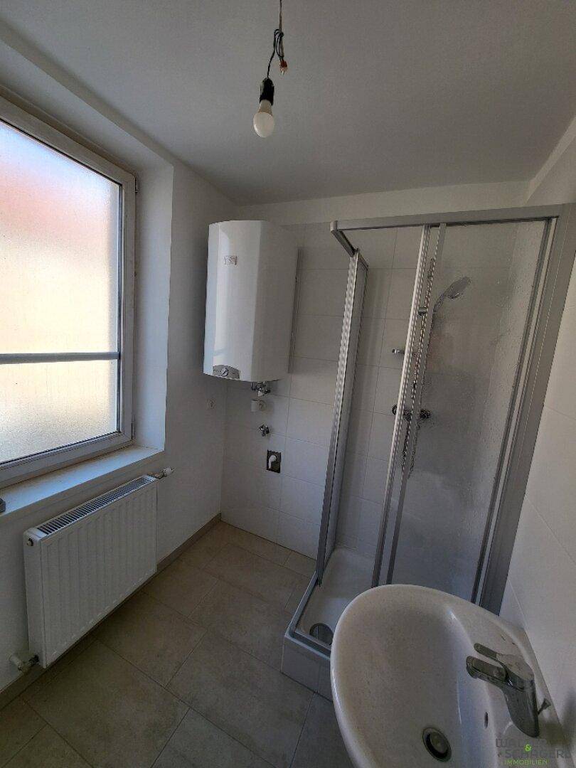 Funktionales Badezimmer mit Duschkabine, Waschbecken, Fenster und Heizkörper, hell gefliest.