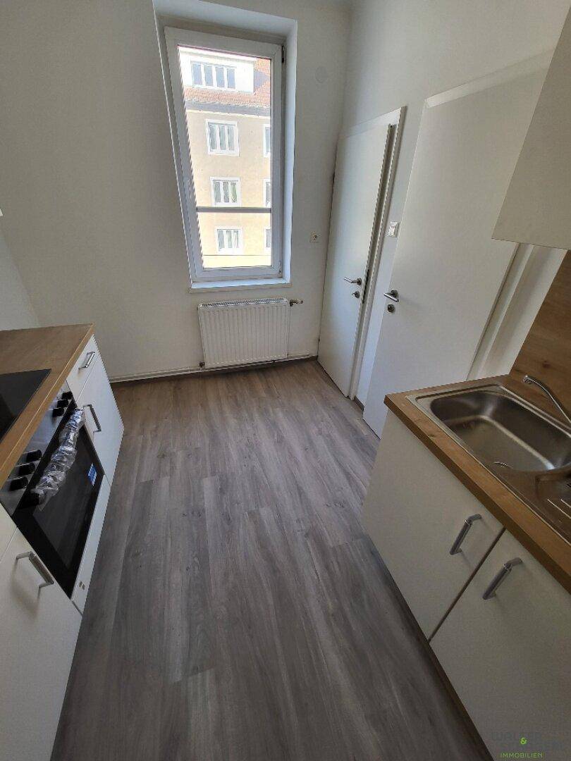 Helle Küche mit Fensterblick auf ein Nachbargebäude, ausgestattet mit Spüle und Arbeitsplatte.