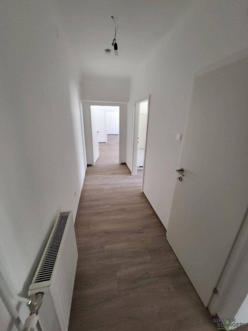 Heller Flur mit Laminatboden, weißen Wänden und Zugang zu verschiedenen Zimmern.