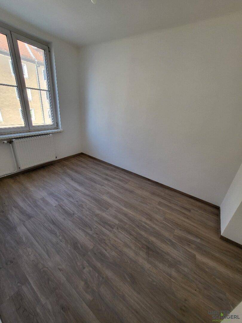 Helles Schlafzimmer mit Laminatboden und einem Fenster, das viel Tageslicht hereinlässt.