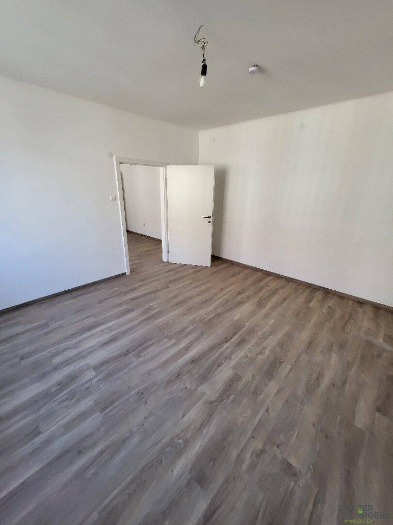 Geräumiges, leeres Zimmer mit hellem Laminatboden und weißen Wänden, bereit zum Einzug.