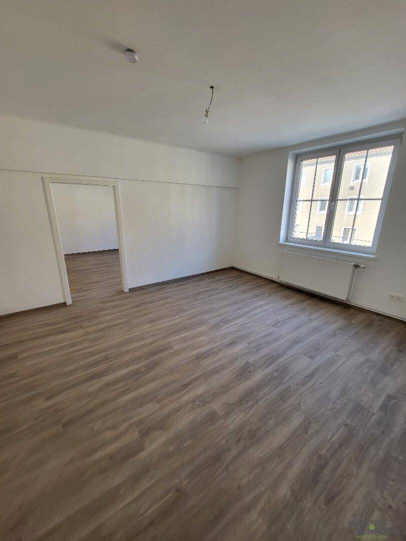 Geräumiges Wohnzimmer mit Laminatboden und großem Fenster, das den Raum mit Licht füllt.