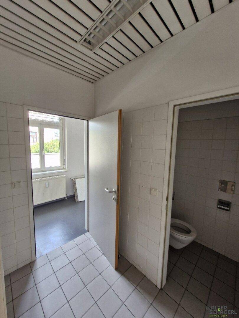 Einfaches Badezimmer mit weißen Fliesen an Wänden und Boden, inklusive Toilette und Heizkörper.