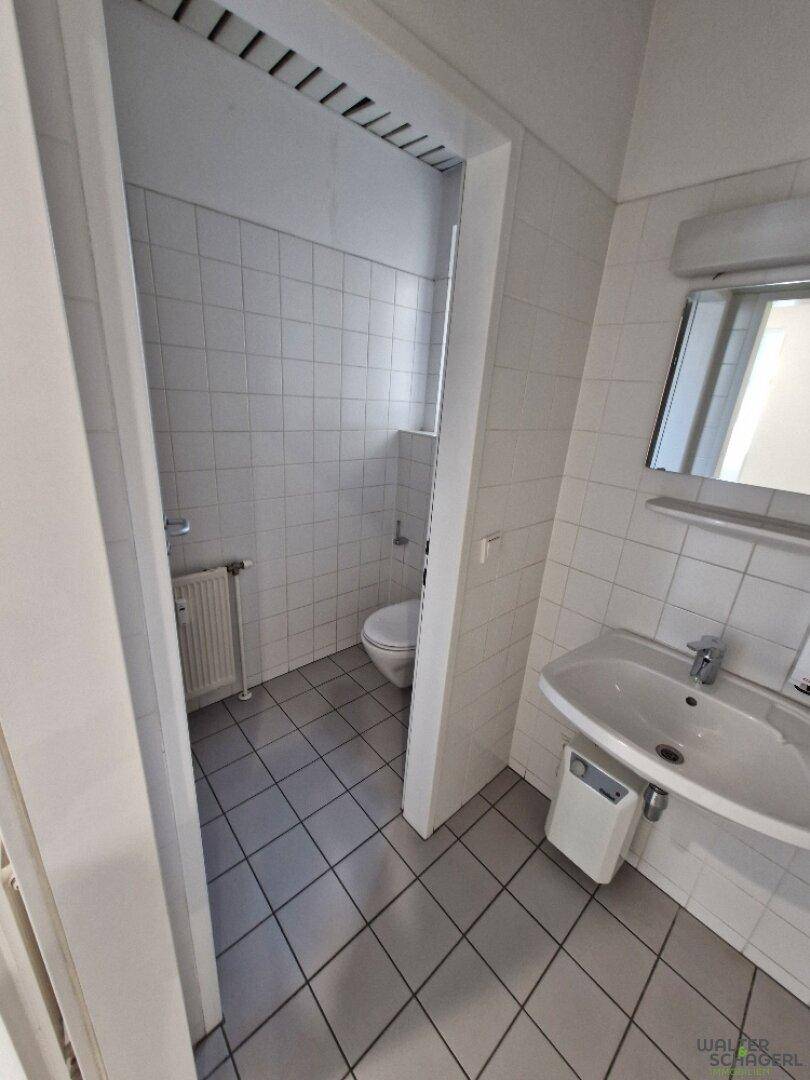 Helles Badezimmer mit weißen Wand- und Bodenfliesen, ausgestattet mit Toilette und Waschbeckenbereich.
