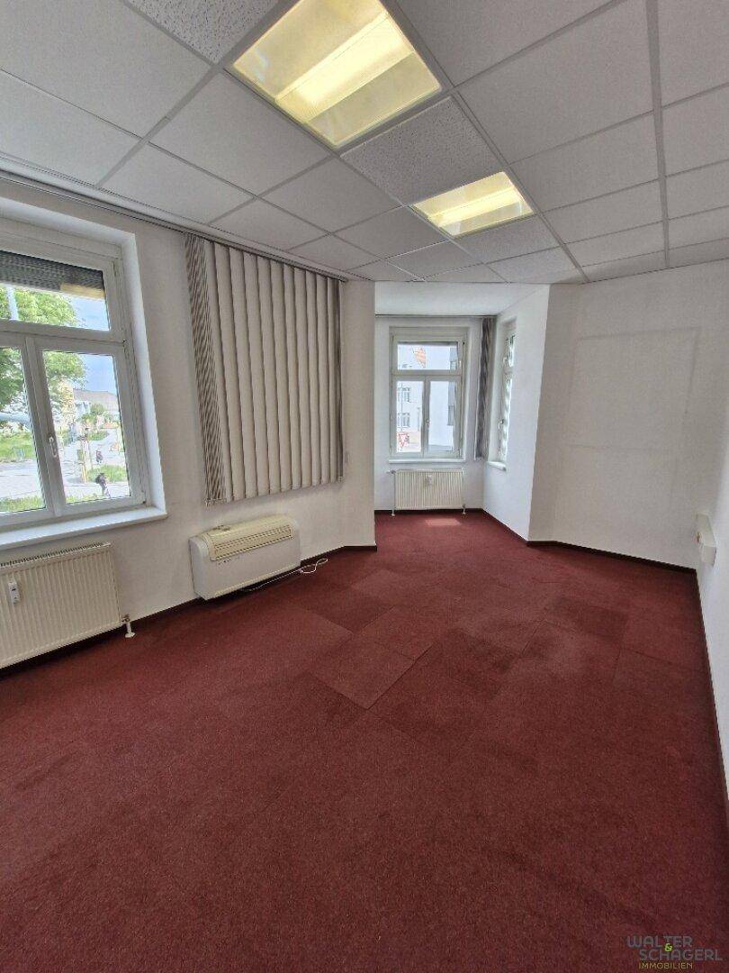 Leeres Büro mit rotem Teppichboden, großen Fenstern und abgehängter Decke, bereit zur Einrichtung.