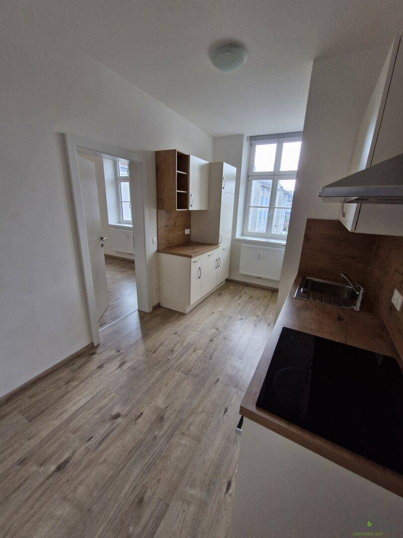 Kompakte Küche mit modernen Geräten, Laminatboden und Blick in einen weiteren Raum.