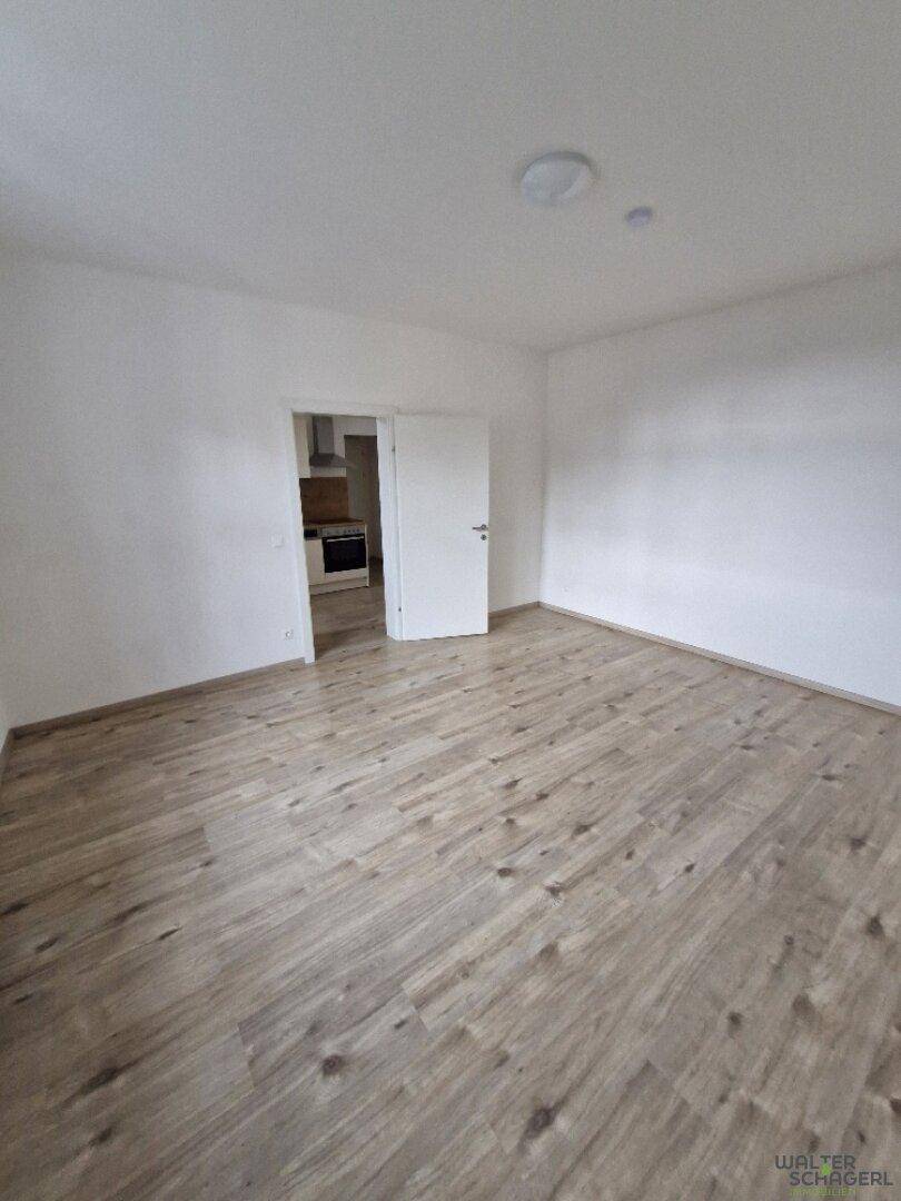 Heller, leerer Wohnraum mit Laminatboden und Zugang zur Küche.