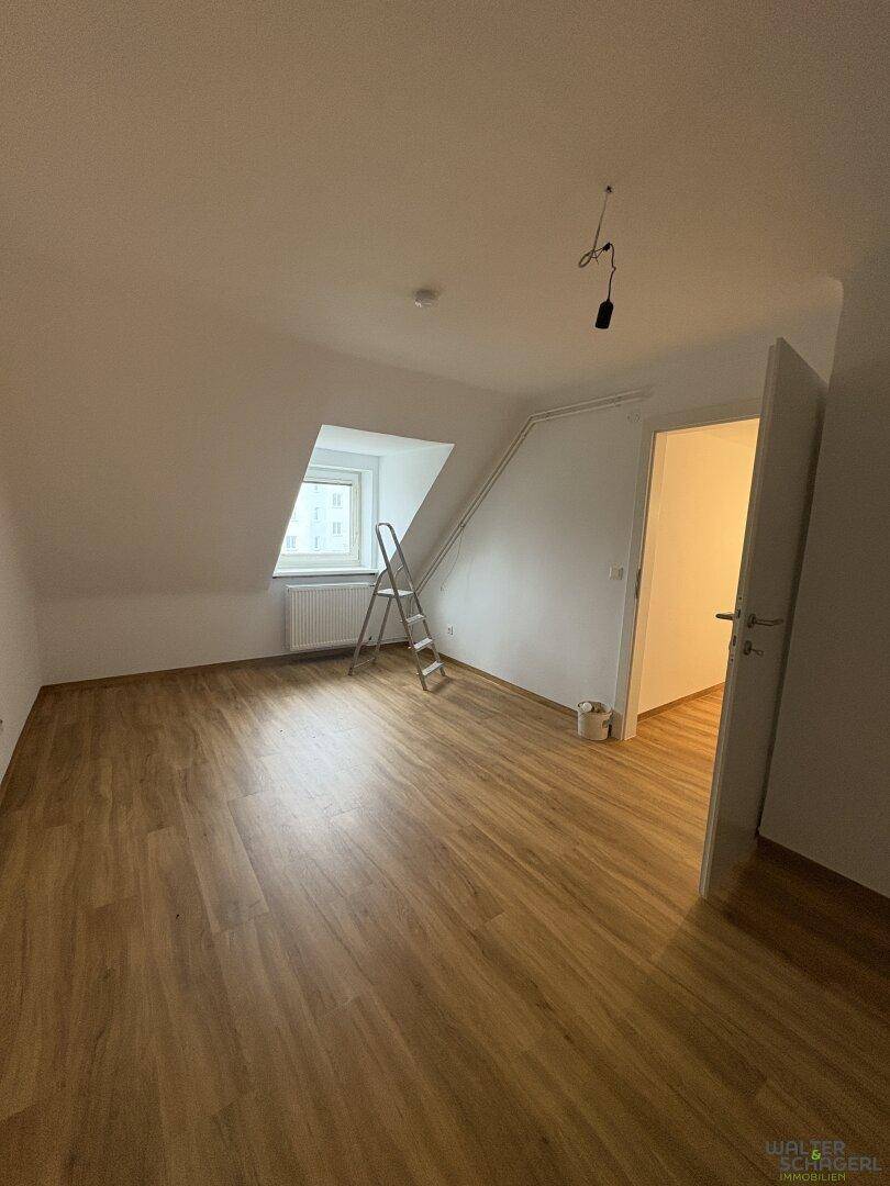Leerer Raum im Dachgeschoss mit Schrägdecke, Laminatboden und Fenster.