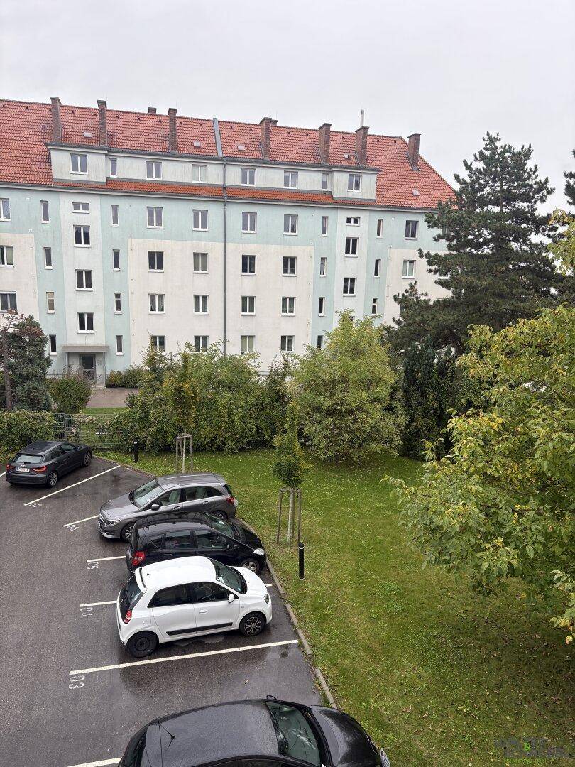 Mehrfamilienhaus mit rotem Ziegeldach, Parkplätzen und Grünflächen im Vordergrund.