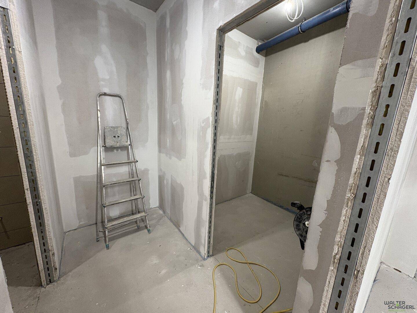 Kleinerer Raum im Rohbau mit Trockenbauwänden und sichtbaren Installationen, eine Leiter steht bereit.