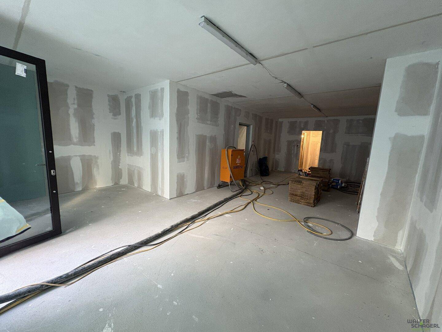 Innenraum im Rohbau mit Trockenbauwänden, Betonboden und Baugeräten während der Renovierung und des Ausbaus.