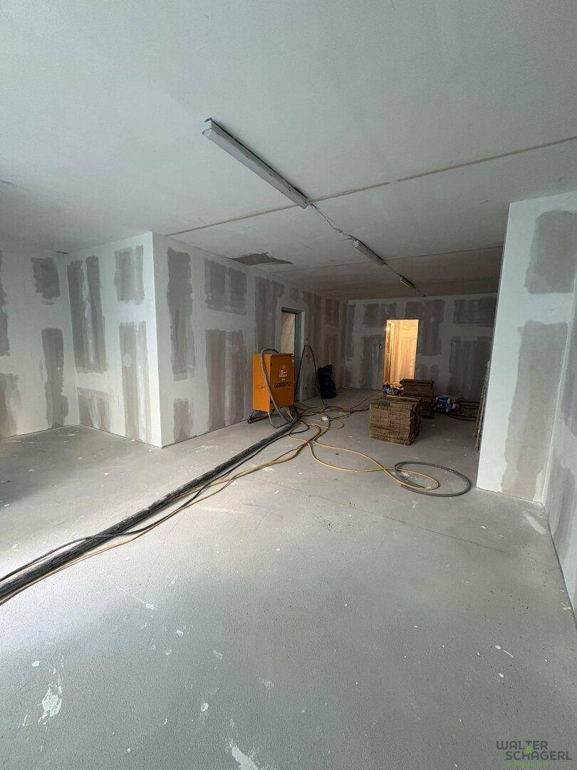 Großer Raum im Rohbau mit unverputzten Trockenbauwänden und Betonboden, bereit für den weiteren Ausbau.