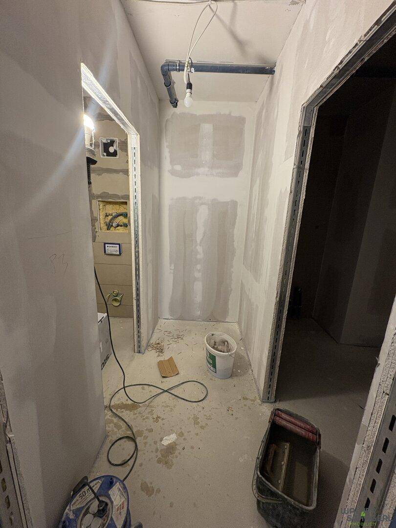 Schmaler Flur oder Technikraum im Rohbau mit sichtbaren Leitungen und unfertigen Trockenbauwänden.