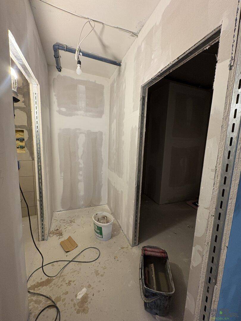 Unfertiger Technikraum mit sichtbaren Rohren an der Decke und Trockenbauwänden im Bauzustand.