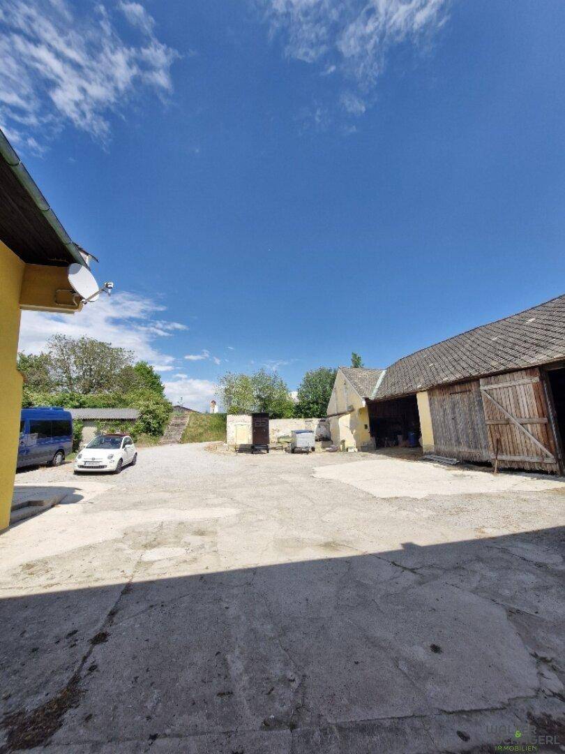 Großer gepflasterter Hofbereich mit Parkplätzen und angrenzenden Wirtschaftsgebäuden unter blauem Himmel.