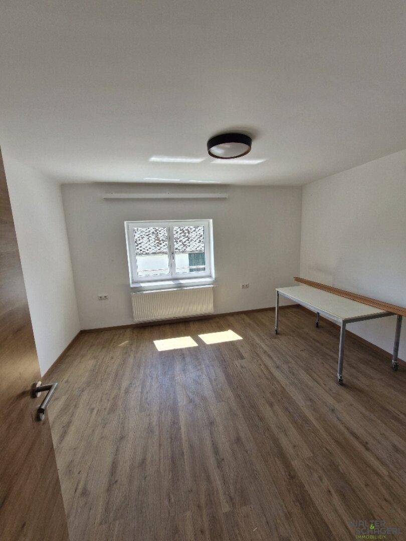 Freundliches Schlafzimmer mit Holzboden, Fenster und einem einfachen Tisch, ideal für ein Büro.
