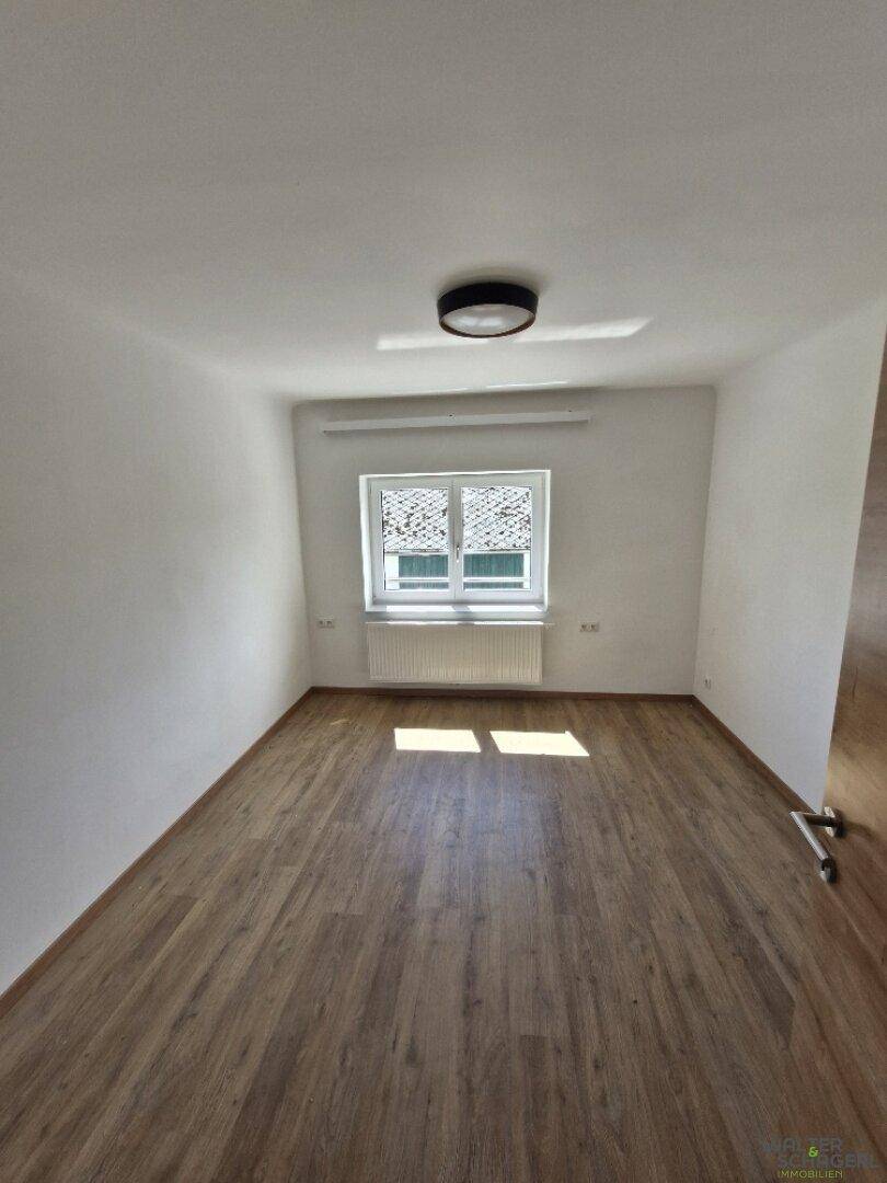 Geräumiges Schlafzimmer mit Laminatboden und großem Fenster, das viel Tageslicht hereinlässt.
