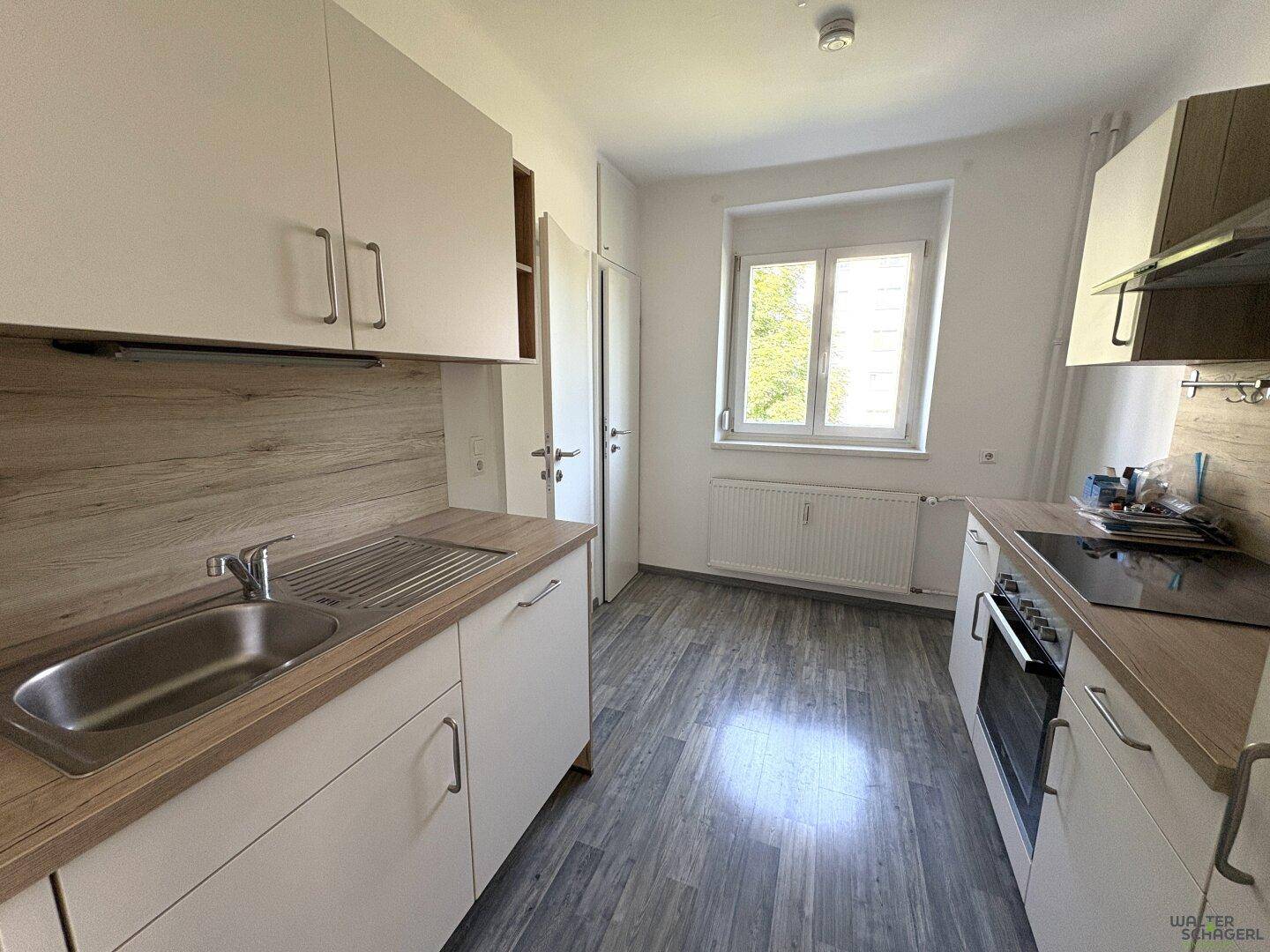 Helle Küche mit Fenster, Heizkörper und funktionalen Einbauschränken in Holzoptik und Weiß.